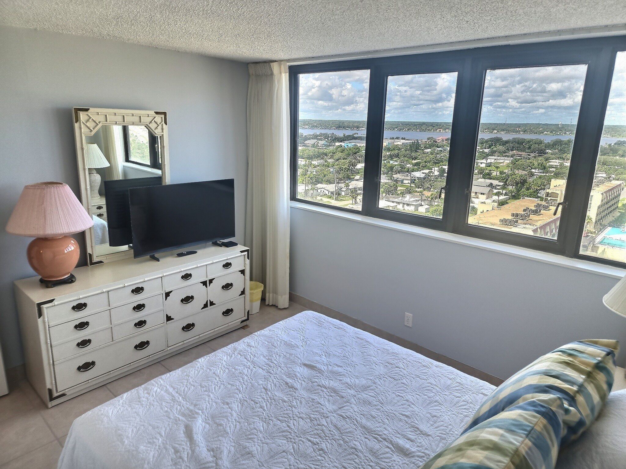 Ein Schlafzimmer mit Bett, Kommode, Fernseher und Fenster mit Blick auf die Stadt.