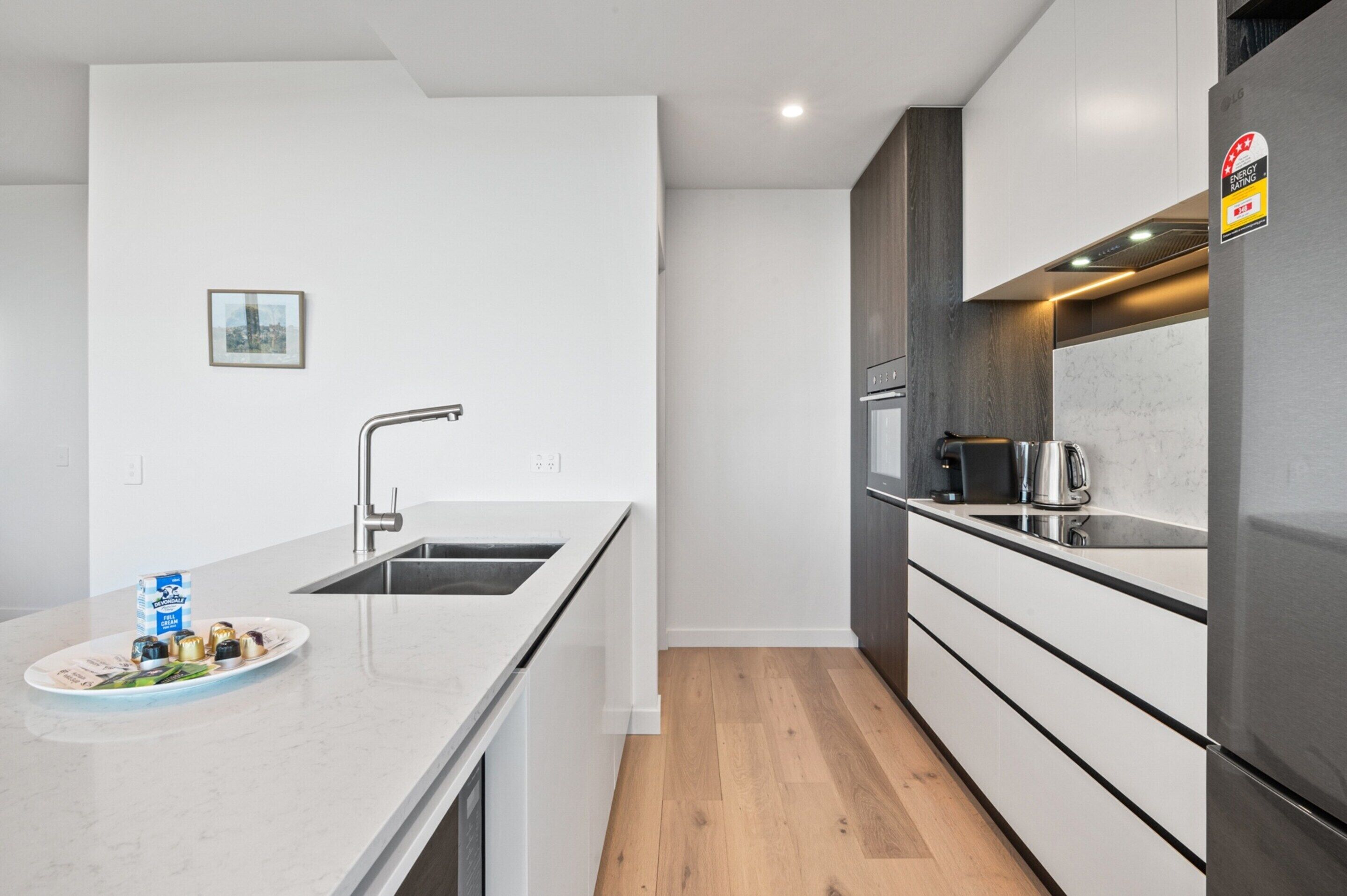 A modern kitchen with white cabinetry, a stainless steel sink, and a wooden floor.