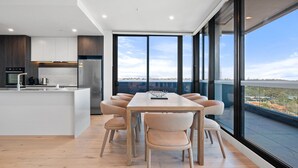 Een moderne keuken met een centraal eiland, grote ramen en een eethoek met stoelen.
