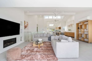 A modern living room with a large flat-screen TV, a glass coffee table, a gray sofa, and a wooden bookshelf.