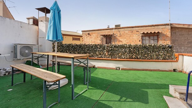 Eine Dachterrasse mit Kunstgras, einer Holzbank, einem Tisch und einem blauen Sonnenschirm.