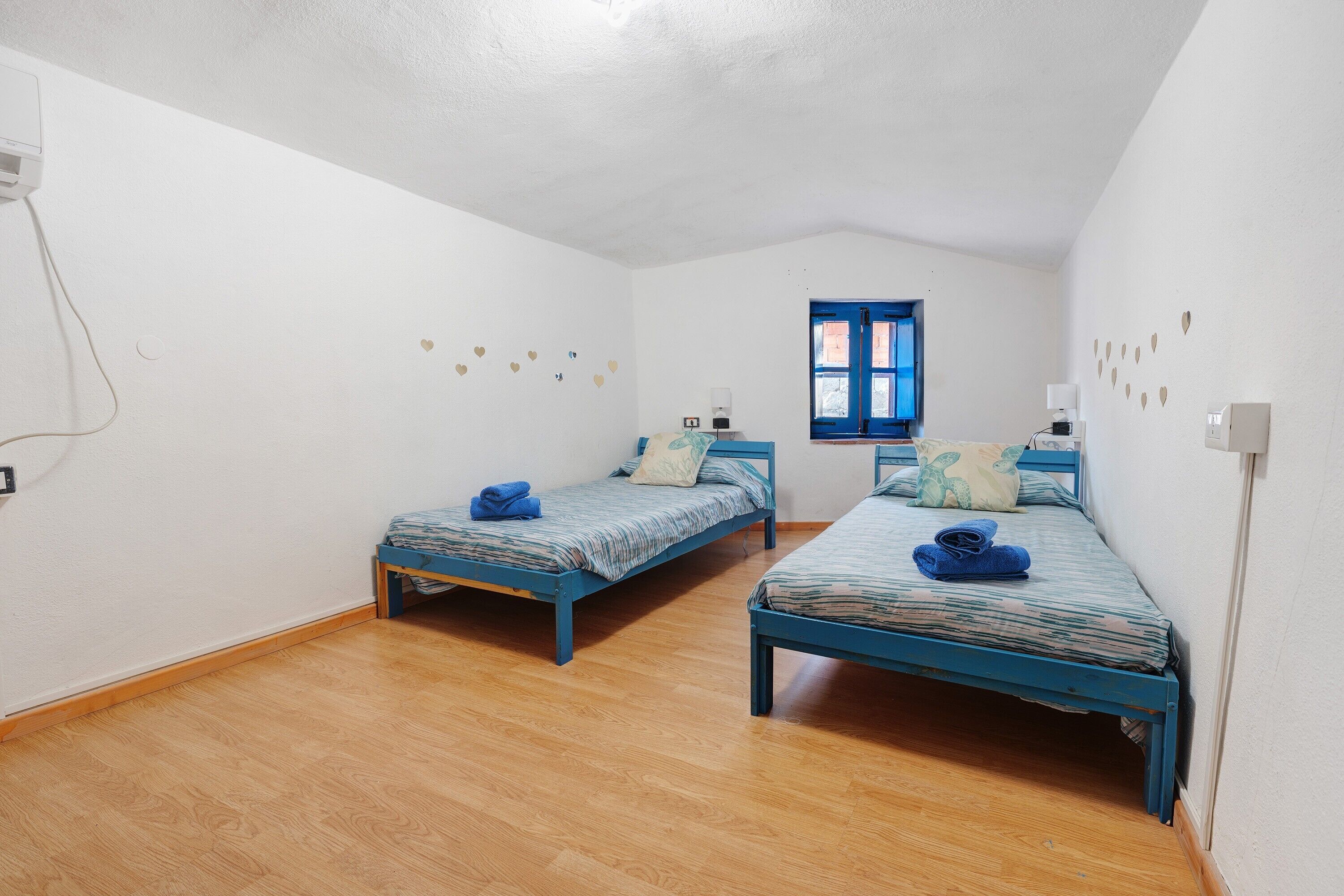 Una habitación con dos camas individuales, una ventana y una lámpara fijada a la pared.
