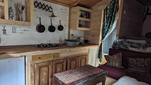 A rustic kitchen with wooden cabinets, a stove, and hanging pots. There is a bench with a patterned tablecloth and a fur throw. - Charming gypsy caravan in green Provence, at La Mauvaise Herbe, Barjols (Barjols)