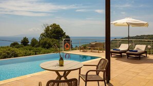 Área da piscina com vista para o mar, mesa, cadeiras e guarda-sóis.