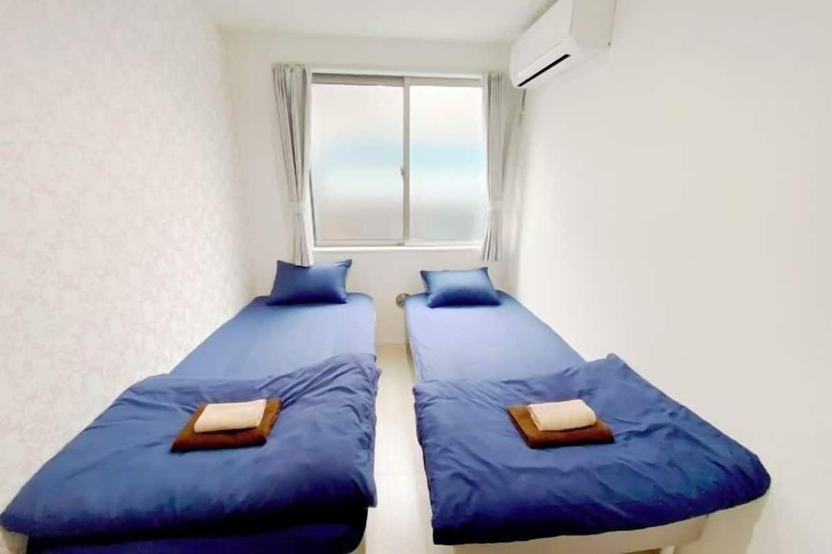 A room with two beds, a window with curtains, and an air conditioner.