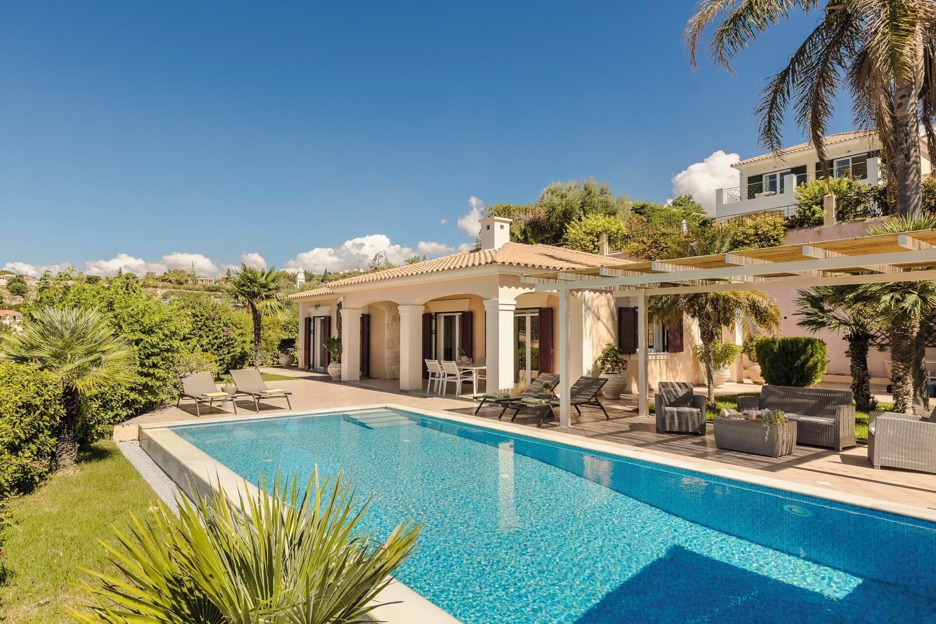 Un espace aménagé au bord de la piscine, avec une piscine à l’eau d’un bleu limpide, des chaises longues et une pergola.