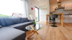 Un salon moderne avec une table basse en verre, un canapé gris et un coin repas comprenant une table et des chaises en bois.