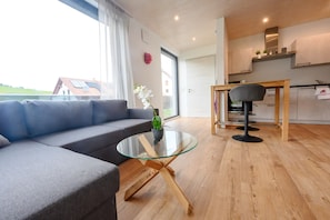 Ein modernes Wohnzimmer mit einem Couchtisch aus Glas, einem grauen Sofa und einem Essbereich mit Holztisch und Stühlen.