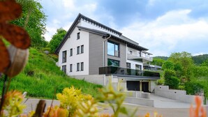 Une maison moderne à deux étages, dotée d’un toit plat, de grandes fenêtres et d’un balcon.
