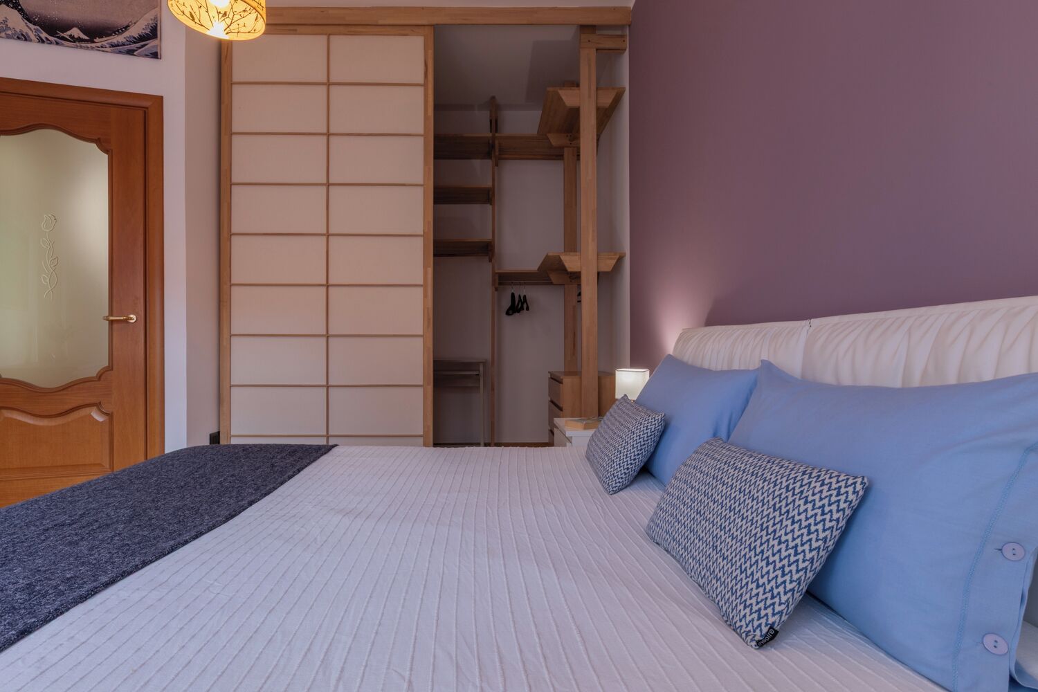 A bedroom with a bed, pillows, a wardrobe, and a sliding door.