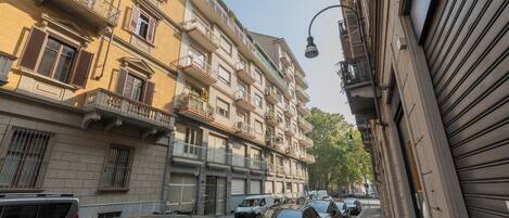 A narrow street with parked cars and multi-story buildings with balconies.