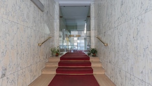 Un escalier au sol de marbre, recouvert d’une moquette rouge, mène à une porte d’entrée en verre.