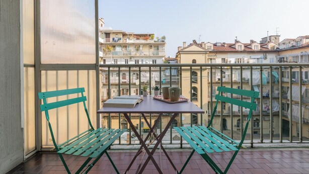 Un balcon avec deux chaises vertes et une table, donnant sur un paysage urbain avec des immeubles.