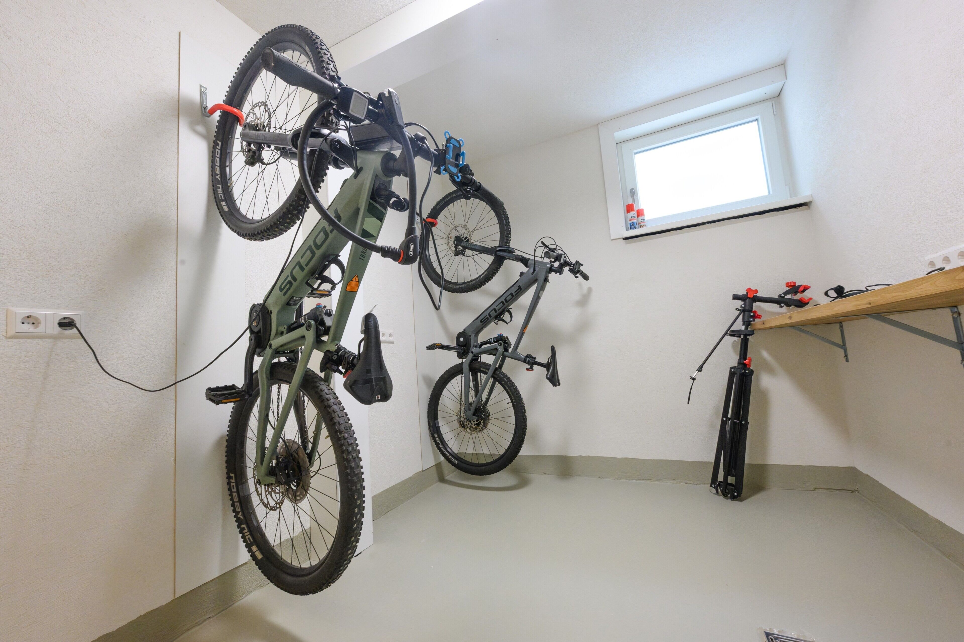A room with two bicycles mounted on a wall, a window, and a shelf with items.