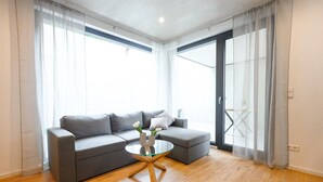 Un salon moderne avec un canapé gris, une table basse en verre et des rideaux légers.
