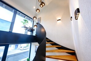 Un escalier moderne avec des marches en bois et une rampe noire, menant à un balcon agrémenté d’un pot de fleurs.