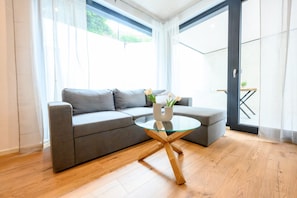 A modern living room with a grey sofa, a glass coffee table, and a wooden floor. - Apartment Bergblick – Modern Comfort with Terrace and Garden View (Kappelrodeck)