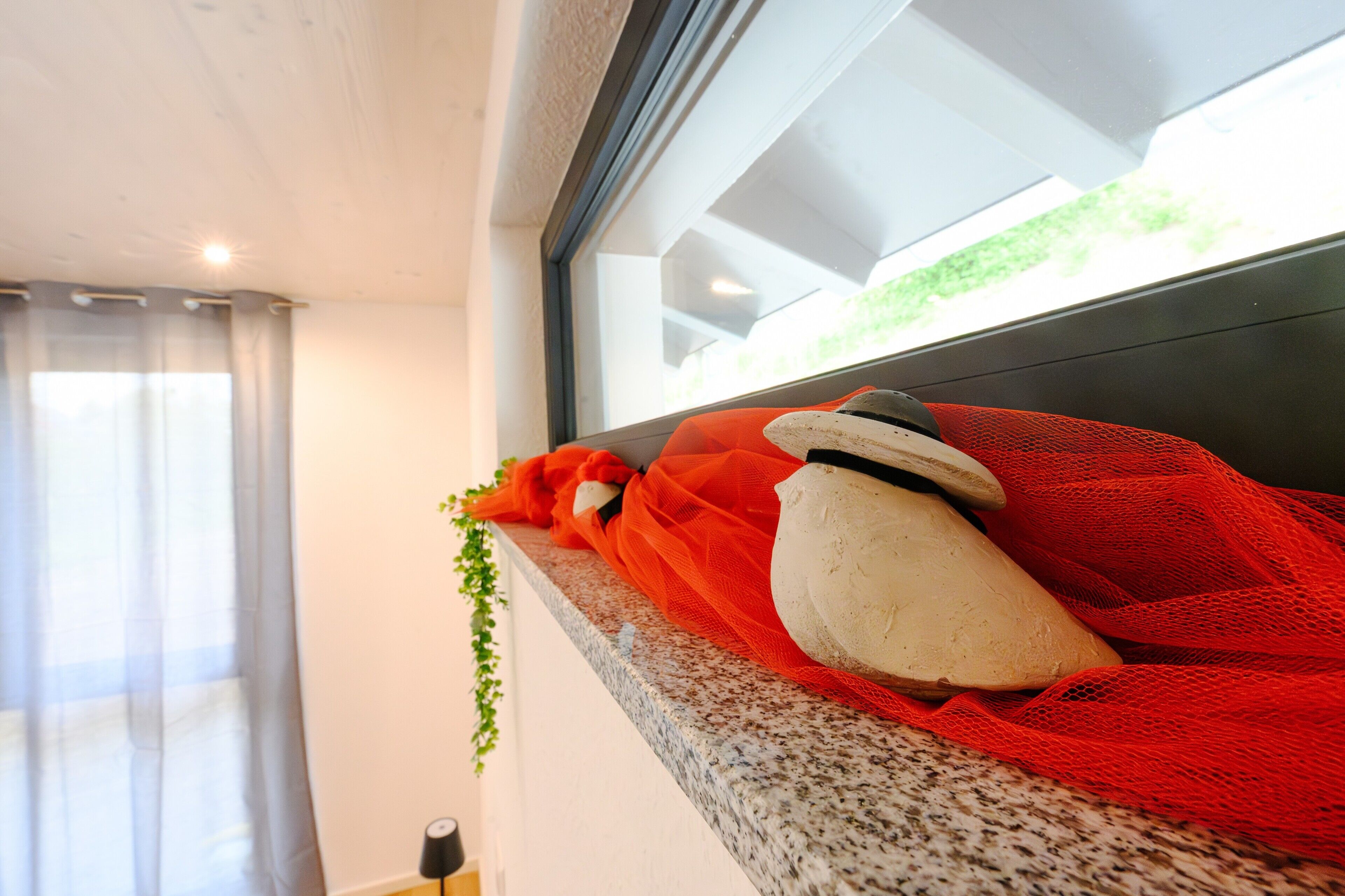 A stone sculpture on a granite ledge, a window with a view of greenery, and a curtain partially drawn.