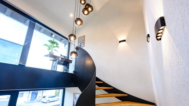 Una escalera moderna con peldaños de madera y barandilla negra, que lleva a un balcón con planta en maceta.