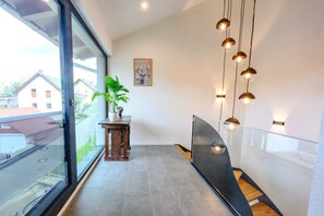 Un interior moderno con un ventanal grande, una planta en maceta, una obra de arte enmarcada e iluminación colgante.