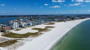 An aerial view of a coastal city with a wide sandy beach, a marina, and a dense cluster of hotels and buildings along the shore.