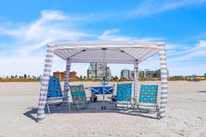 A beach cabana with striped awnings and beach chairs with floral patterns.
