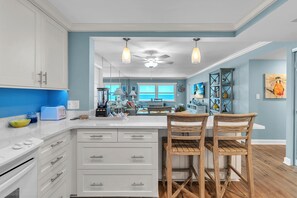A modern kitchen with white cabinets, a large island, and wooden chairs.