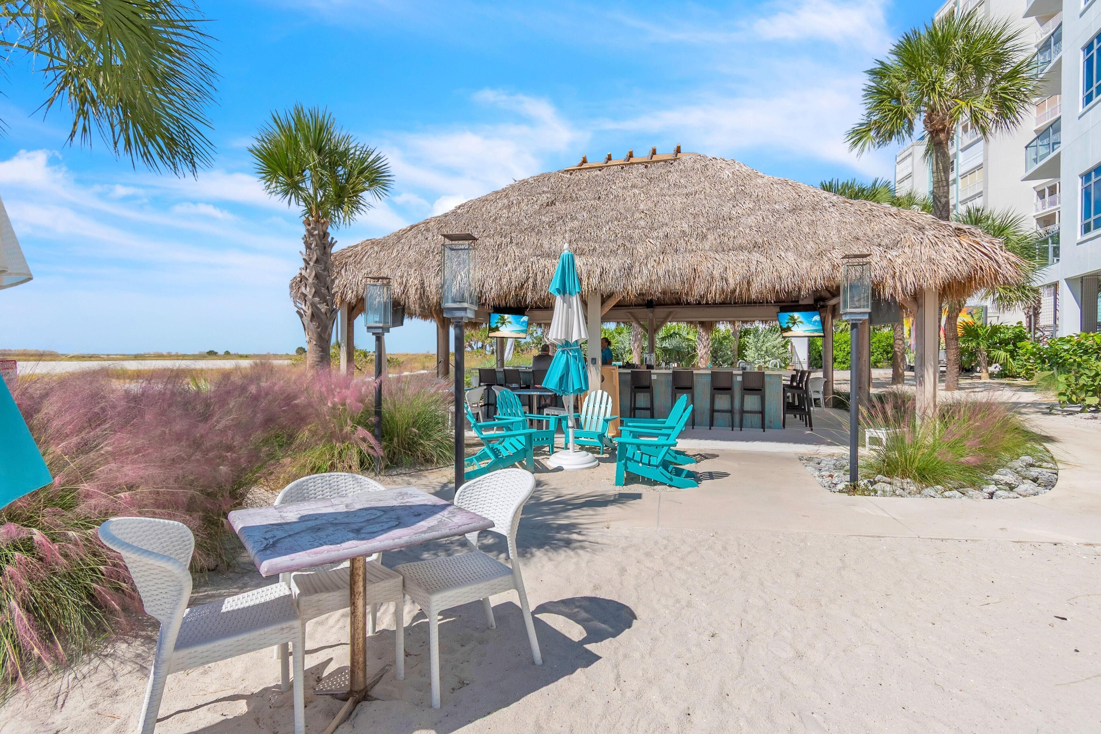 Eine Terrasse direkt am Strand mit Strohdach, weißen Stühlen und einem Tisch.