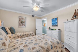 A bedroom with two beds, a ceiling fan, a dresser, and artwork on the walls.
