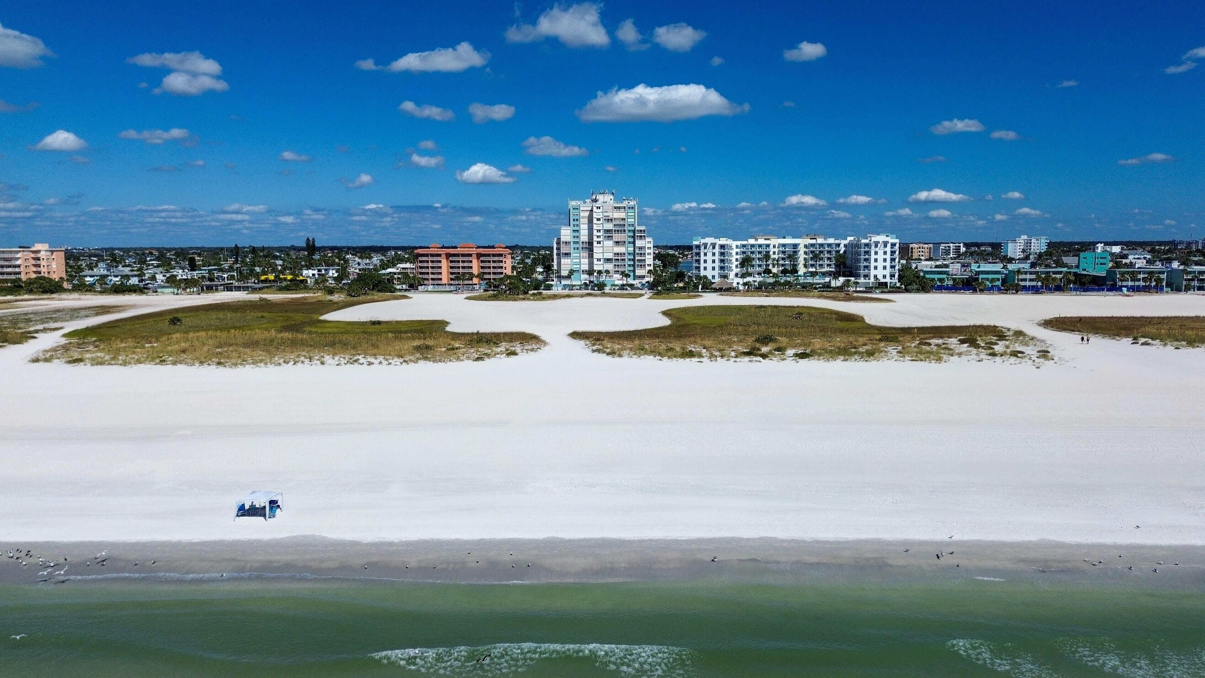 A coastal area with a sandy beach, a marina, and several multi-story buildings in the background.