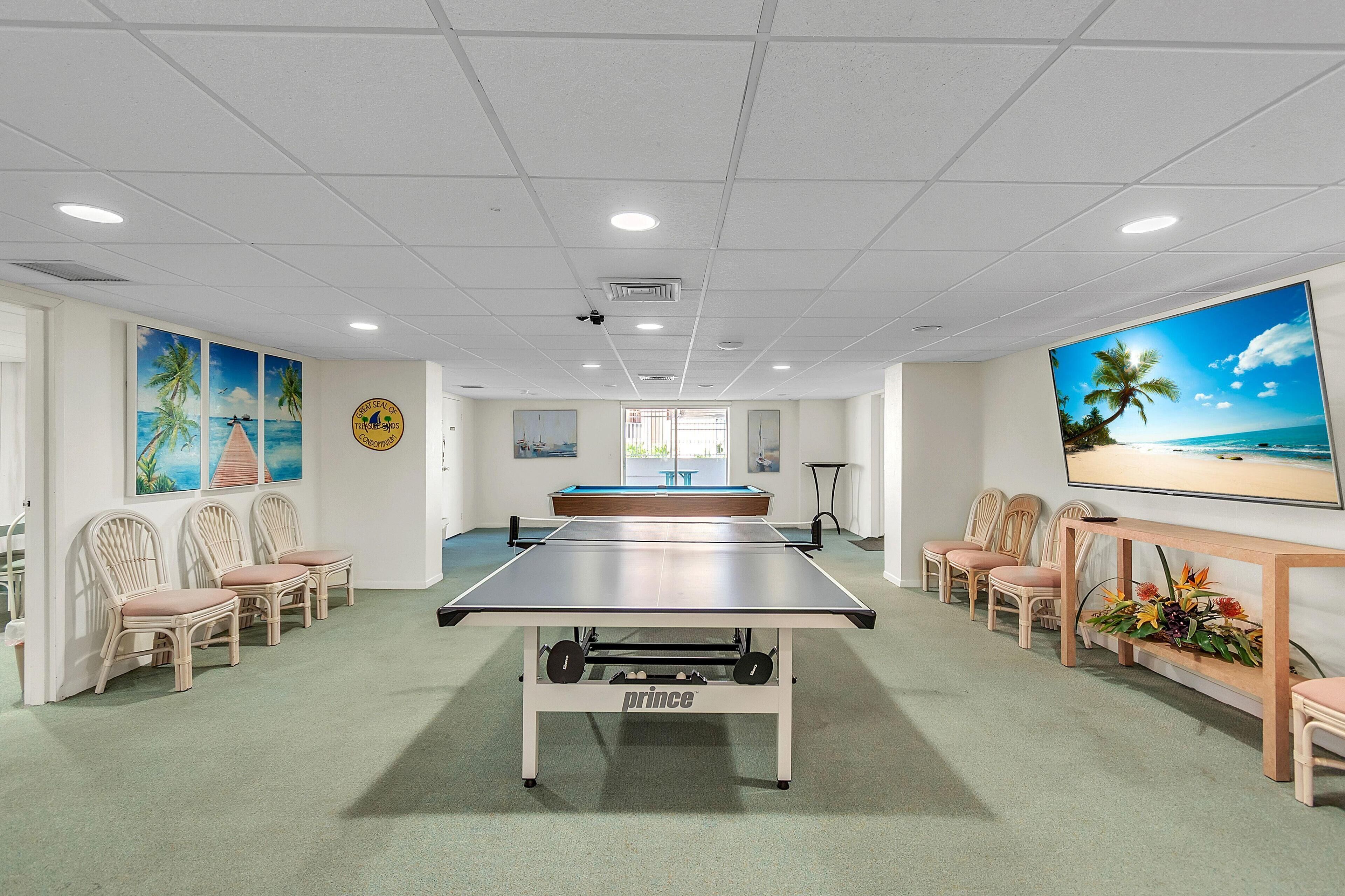 A spacious room with a ping pong table, comfortable seating, and beach-themed artwork on the walls.