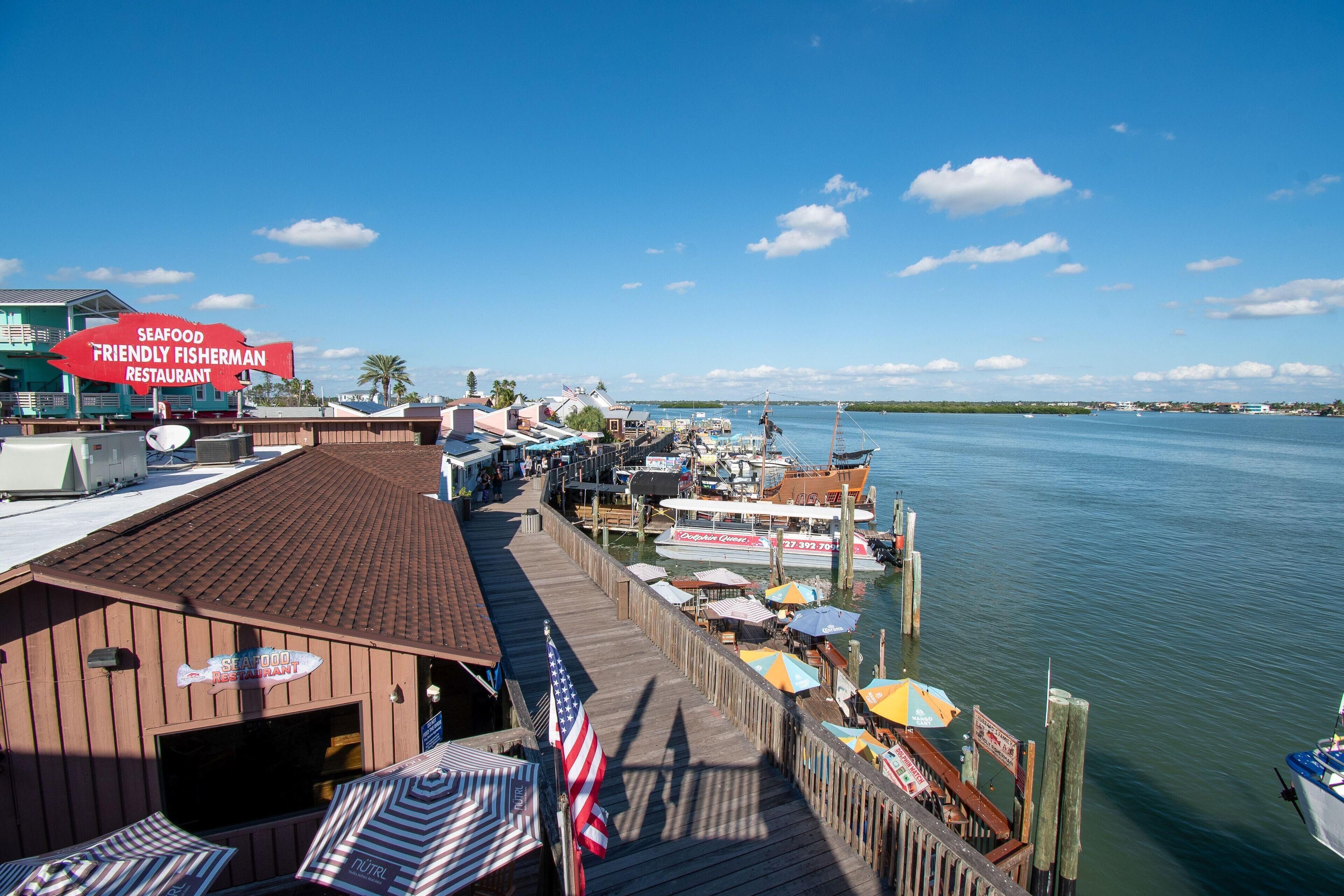 A waterfront restaurant with a wooden deck, outdoor seating, and a view of the marina.