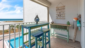 A balcony with a pool, a table, and a hanging light fixture. - Treasure Sands #502 (Treasure Island)