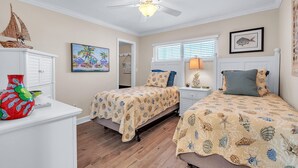 A bedroom with two beds, a ceiling fan, a painting, and a window with blinds. - Treasure Sands #502 (Treasure Island)