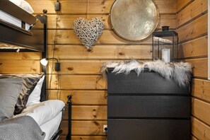 A wooden cabin interior with a bed, a dresser, a wall-mounted heart-shaped decoration, and a round mirror. - Trysil Ski-in/out Chalet and Hot Tub (Trysil)