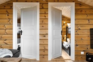 A wooden cabin interior with two white doors, a bed, a table, and a lamp. - Trysil Ski-in/out Chalet and Hot Tub (Trysil)