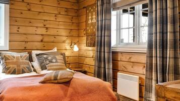 A wooden cabin bedroom with a bed, pillows, a wall-mounted light, and a window with curtains.