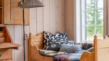 A wooden bed with patterned pillows, a hanging lamp, and a window with a view of greenery.