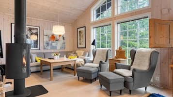 A cozy living room with a fireplace, wooden walls, and large windows.