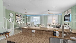 Una cocina moderna con encimeras de granito, un lavamanos de acero inoxidable y una zona de comedor con una mesa y sillas blancas.