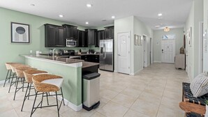 Una cocina moderna con armarios oscuros, un refrigerador de acero inoxidable y una zona de bar con taburetes de mimbre.