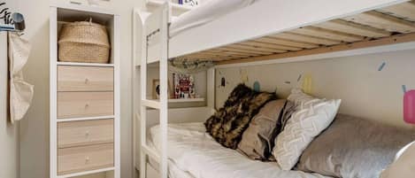 A bunk bed with a storage unit beside it, a wall-mounted shelf with a book, and a small decorative item.