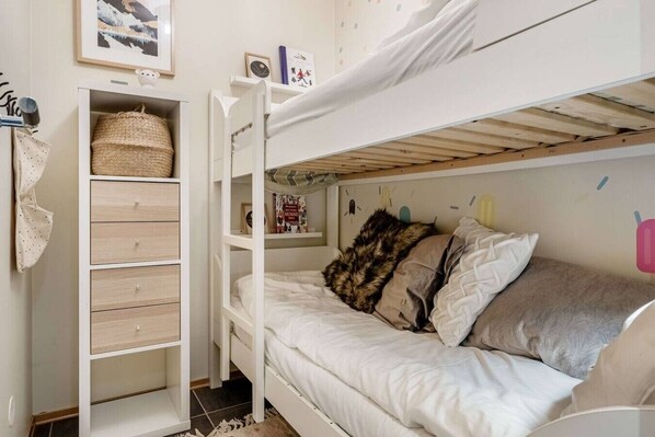 A bunk bed with a storage unit beside it, a wall-mounted shelf with a book, and a small decorative item.