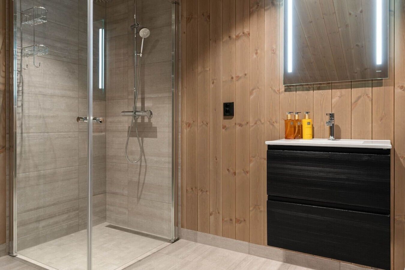 A modern bathroom with a glass-enclosed shower, a wooden vanity with a black drawer, and a mirror above the sink.
