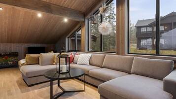 A modern living room with a sectional sofa, a round coffee table, and large windows offering a view of a house.