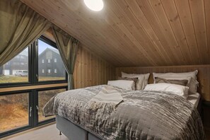 Quarto com cama grande, teto de madeira e janela com cortinas.
