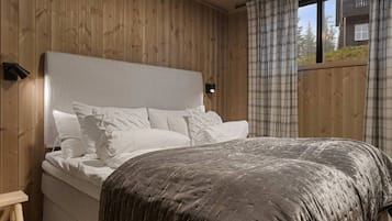 A bed with a headboard, pillows, and a blanket in a room with wooden walls and a window.