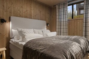 Una cama con cabecera, almohadas y una manta en una habitación con paredes de madera y un ventanal.