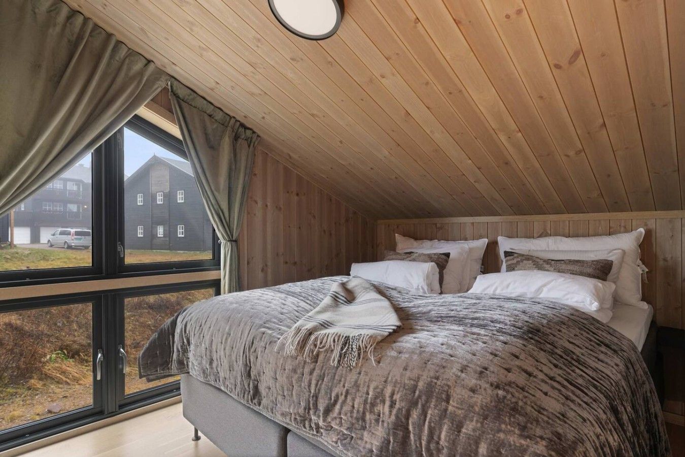 Une chambre avec un grand lit, un plafond en bois et une fenêtre donnant sur un immeuble.