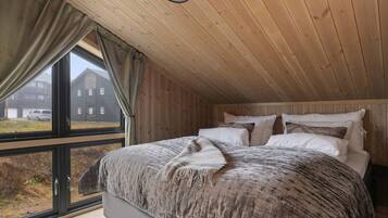 Een slaapkamer met een groot bed, houten plafond en een raam met uitzicht op een gebouw.